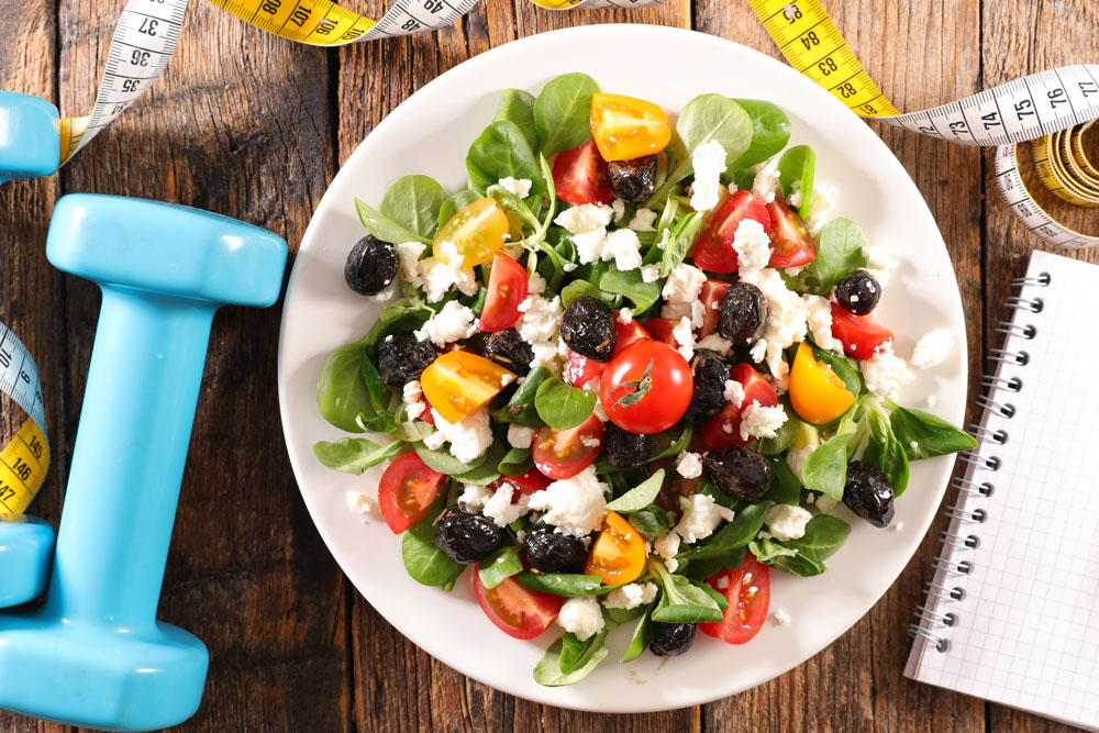 Small weights, healthy salad, and a notebook on a table