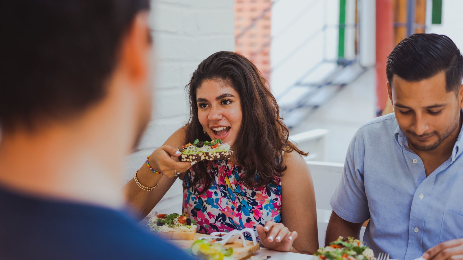 Three friends eating and talking together at an outdoor restaurant table in daylight